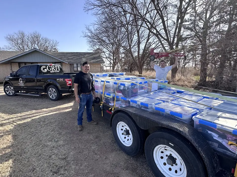GRIT trailer stacked with bins and debris next to a GRIT pickup on a rural property
